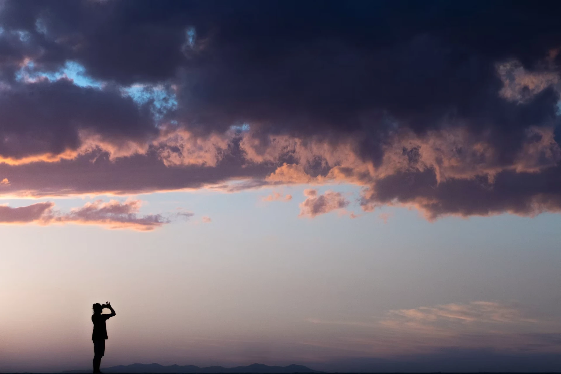 Person silhouetted against a wide sunset sky, looking ahead